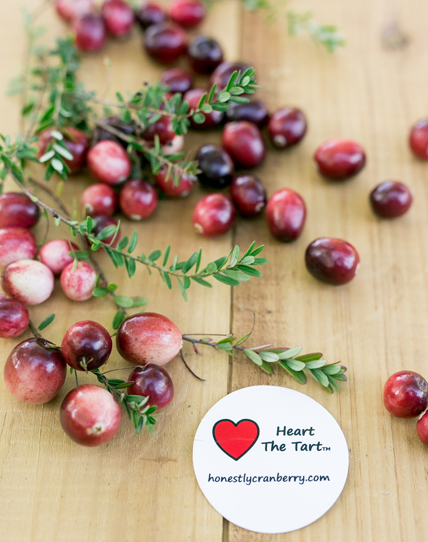Fresh cranberries with green leaves on a wooden surface.